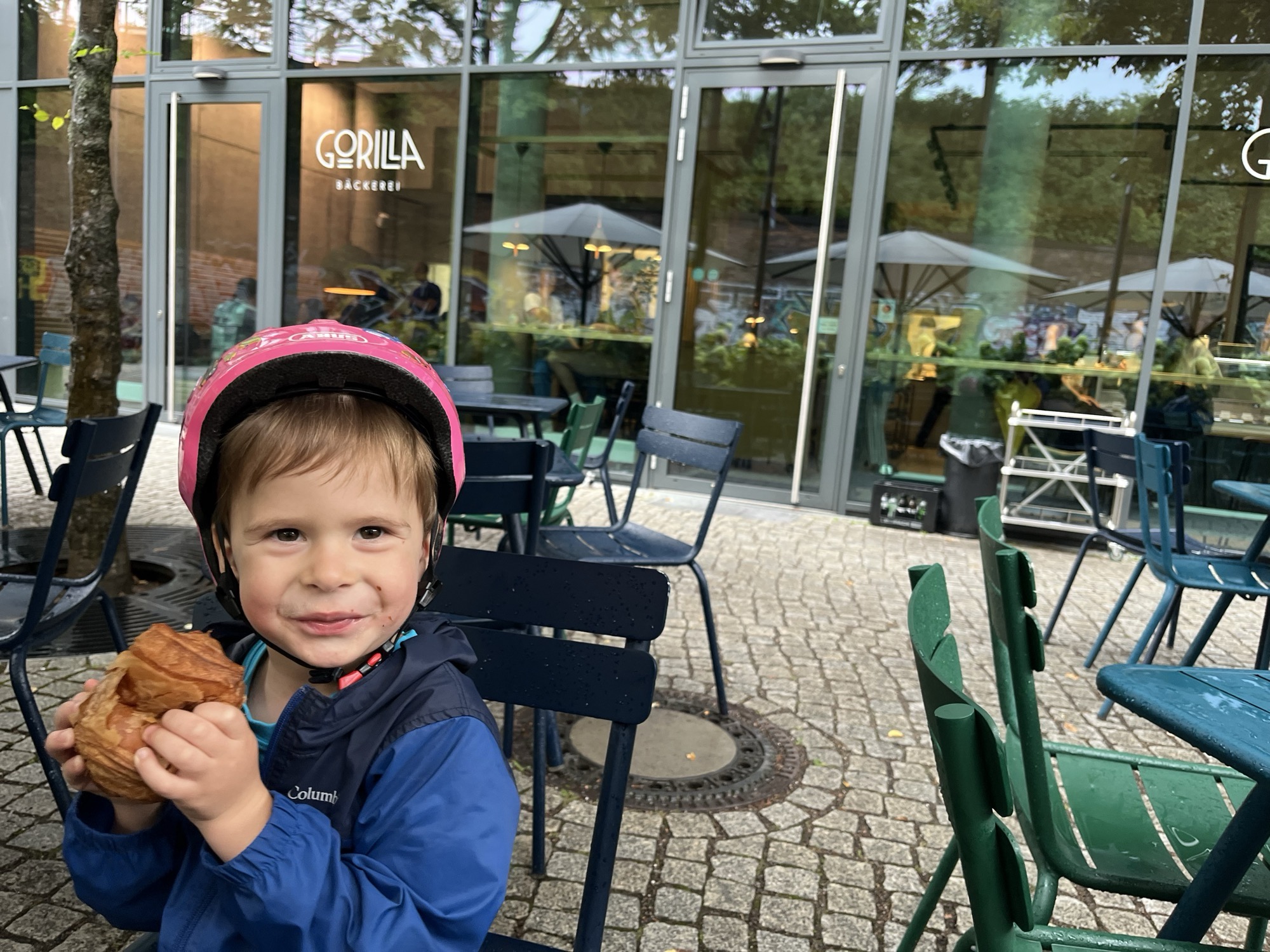George in his pink bike helmet outside Gorilla Bäckerei, croissant in hand