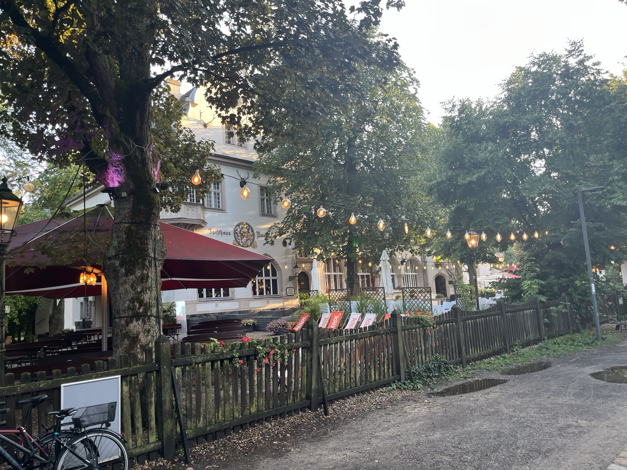 The castle-like building of 12 Apostoli, string lights strung over the biergarten tables behind a wooden fence