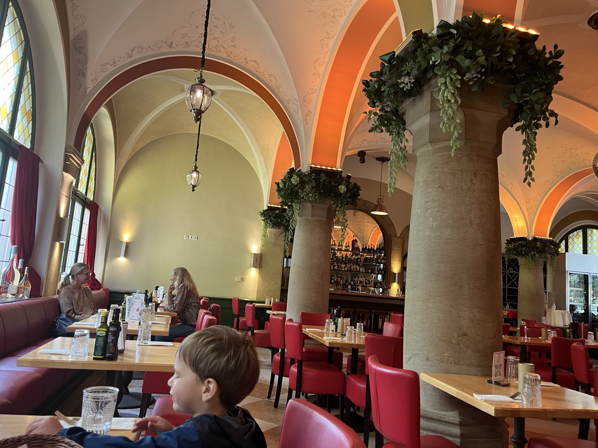 The vaulted dining room at 12 Apostoli, George at our table beneath stone columns draped in greenery