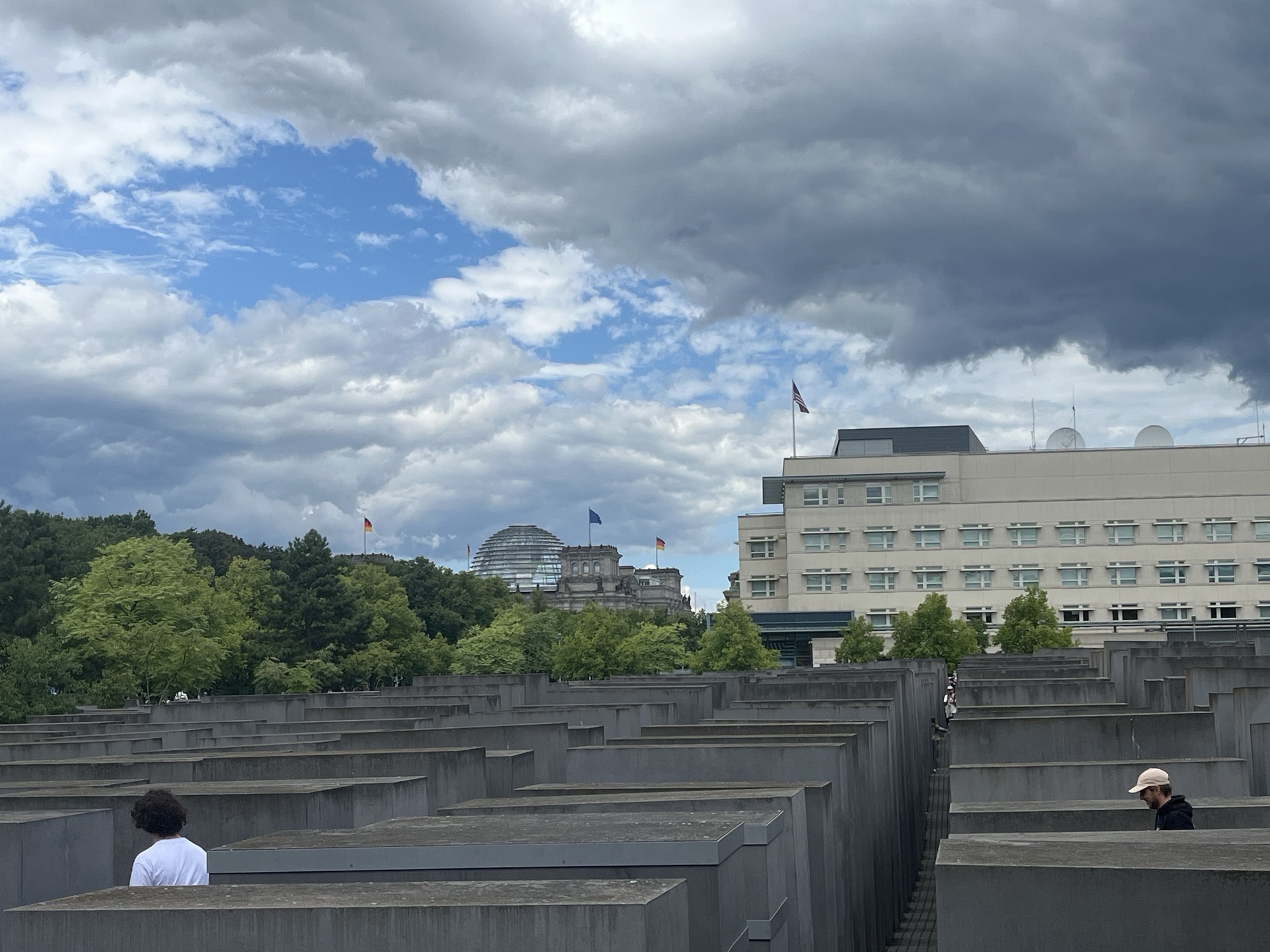 The view from inside the Holocaust Memorial: rows of concrete stelae, with the U.S. Embassy at right and the Reichstag dome rising behind the trees